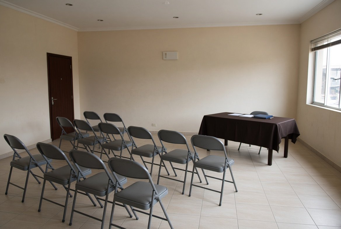 Sala preparada para una junta de vecinos, con las sillas dispuestas y la mesa de la presidencia